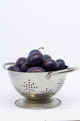 Plums in a colander, separated, close up. White background.