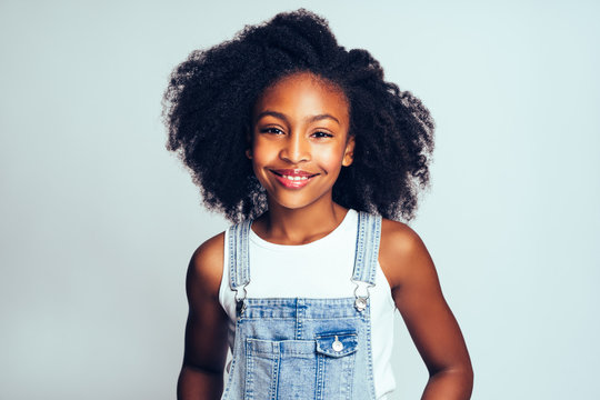 Young African Girl With Long Curly Hair Wearing Dungarees And Smiling  Confdiently While Standing Against A Gray Background Stock Photo, Picture  and Royalty Free Image. Image 97377269.