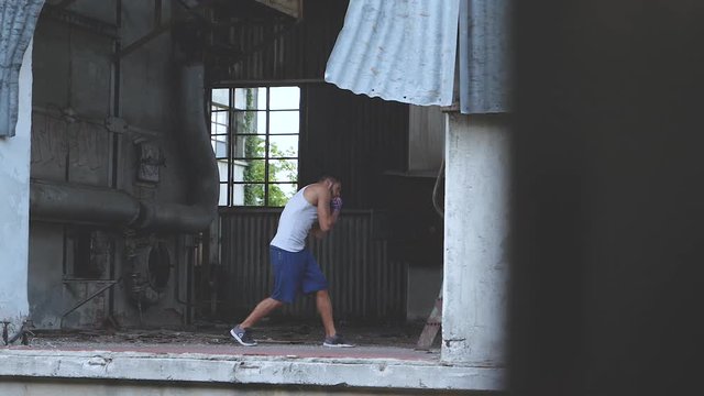 Fit male boxer doing shadow boxing exercise in an old abandoned factory. Ideal for sequence transitions.