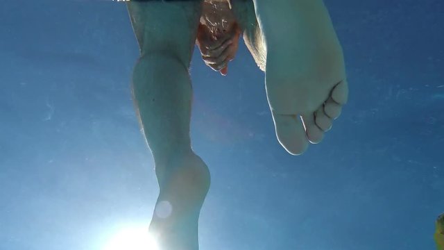Young man sitting on the edge of the pool and moves his feet.