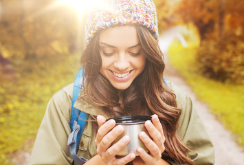 smiling young woman with cup and backpack hiking