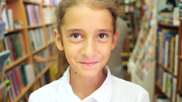 Portrait of a girl 8 - 12 years old, standing in the library. Bookshelves of a bookcase in the background. 4k, slow motion