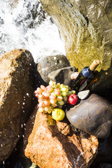 a bottle of wine and fruits among the stones by the sea