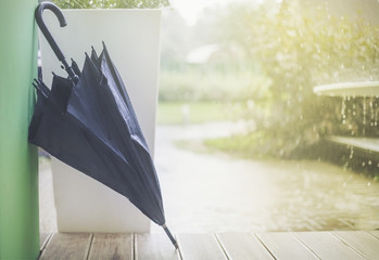 мокрый сложенный темный зонтик на веранде на фоне дождя - obrazy, fototapety, plakaty