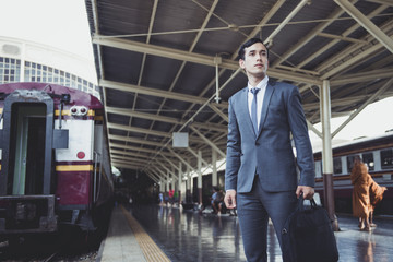 Business man stand close to railway at vintage trainstation with train and people in background