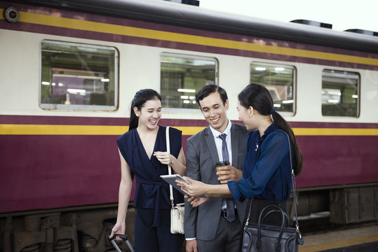 group of people laugh and look at tablet at railway station