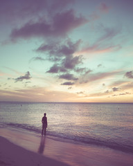 Silhouette lone man at waters edge along beach at sunset.