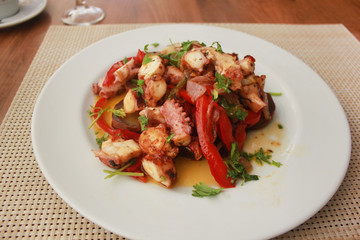 Fototapeta na wymiar Seafood meal with fresh grilled octopus, sweet potatoes,onions, red bell pepper and parsley at restaurant set up table background. Delicious tasty small appetizer served on white plate for dinner. 