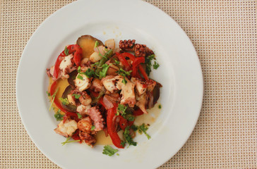 Grilled seafood homemade meal with octopus, sweet potatoes, onions, red bell pepper and parsley. Sea food, vegetables delicious healthy fresh appetizer isolated on white plate at table set for dinner