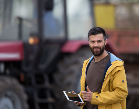 Farmer Holding Tablet With Tractor Behind