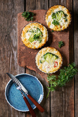 Baked homemade quiche pie in mini metal forms served with fresh greens, plate and cutlery on...