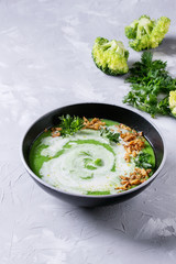 Vegetarian broccoli cream soup served in black bowl with cream, fried onion, fresh parsley and broccoli over over gray concrete background. Top view with space. Healthy eating.