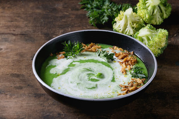 Vegetarian broccoli cream soup served in black bowl with cream, fried onion, fresh parsley and broccoli over old wooden background. Close up. Healthy eating.