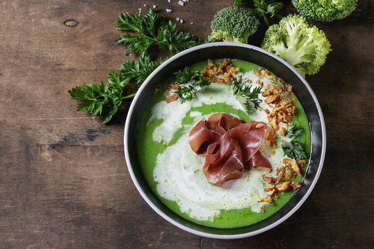 Vegetable broccoli cream soup served in black bowl with italian bresaola ham cream, fried onion, fresh parsley and broccoli over old wooden background. Top view with space. Healthy eating.