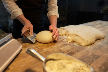 baker portioning dough with bench cutter at bakery