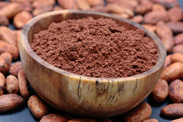 Many cacao beans with powder in a bowl on slate