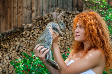 Beautiful girl with red hair on nature with a rabbit in her hands