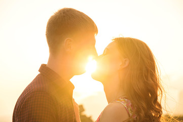 Young happy couple kissing in nature against the setting sun at sunset.