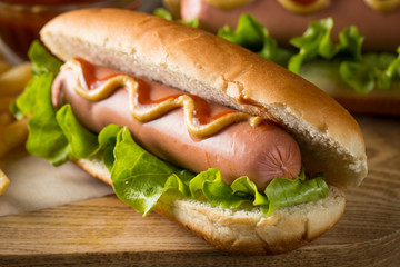 Tasty barbecue grilled hot dog with salad,yellow mustard, onion, ketchup, and French fries on wooden background. Junk and fast food concept.