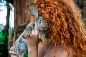 Beautiful girl with red hair on nature with a rabbit in her hands