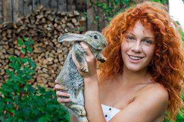 Beautiful girl with red hair on nature with a rabbit in her hands