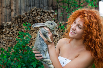 Beautiful girl with red hair on nature with a rabbit in her hands