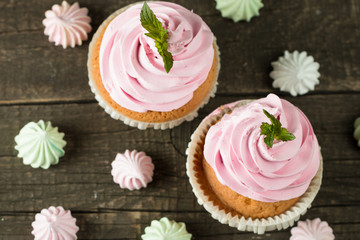 Closeup of cupcakes with vanilla, berries, pink and white cream, chocolate and sprinkles on wooden background. Selective focus. Sweet dessert tasty food concept muffin.