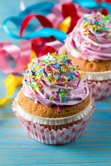 Closeup of cupcakes with vanilla, berries, pink and white cream, chocolate and sprinkles on wooden background. Selective focus. Sweet dessert tasty food concept muffin.