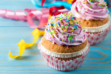 Closeup of cupcakes with vanilla, berries, pink and white cream, chocolate and sprinkles on wooden background. Selective focus. Sweet dessert tasty food concept muffin.