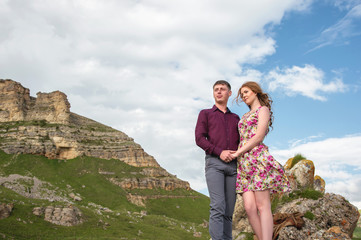 couple Young guy with a girl holding hands standing and looking away in the background of a beautiful landscape of rocks and clouds