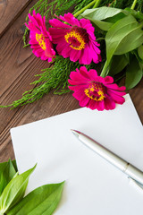 Pink flowers of the zini and sheet of paper for text on a wooden background with copy space in a rustic vintage style