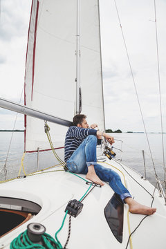 man in striped sweater sits on white sailing yacht