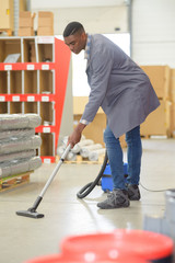 young male janitor cleaning floor with vacuum cleaner
