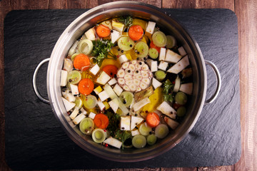 Broth with carrots, onions various fresh vegetables in a pot - colorful fresh clear spring soup. Rural kitchen scenery vegetarian bouillon or stock