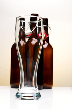 Empty beer glass with beer bottles on white background