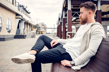 young guy with a beard and mustache posing on the street in the sunlight, fashion man, style, vintage style, retro men, handsome beard, outdoor portrait, hipster man