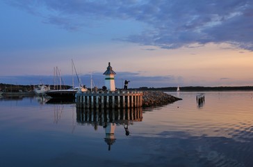 Small lighthouse and sailing boats at sunset.
