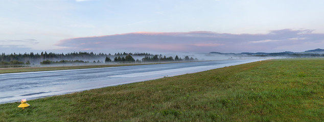 Empty runway at airport during a foggy sunrise