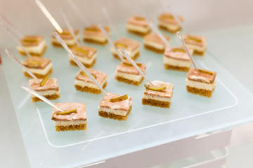 Small snacks canape with brisket, rye bread, omelet and lettuce on skewer on a plate.