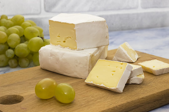 Camembert or brie cheese on a wooden board and green grapes