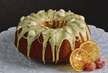 Danish carrot cake with icing and candied fruit on white tablecloth with black background