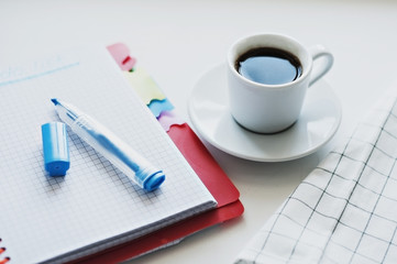 A cup of coffee with notepad on a white table. Not isolated.