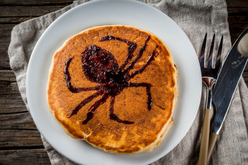 Ideas for breakfast are Halloween, food for children. Pumpkin pie pancakes decorated with chocolate syrup in a traditional style - spider web, spider, jack lantern. On wooden rustic table, copy space