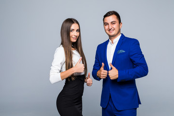 Two confident smiling businesspeople in formalwear showing thumbs-up on gray background