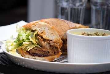Lunch combo included crispy fresh sandwich with lettuce, sauce and meat and soup on the side served on a table outside. Close-up.
