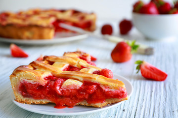 Plate with piece of delicious strawberry cake on white wooden table