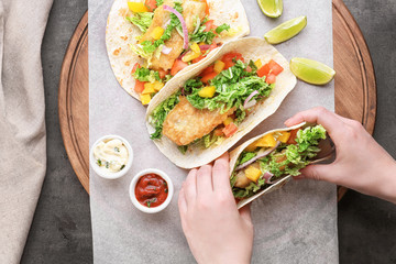 Woman holding delicious fish taco in kitchen