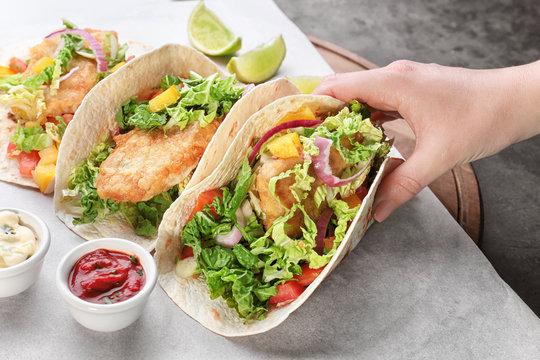 Woman holding delicious fish taco in kitchen
