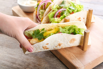 Woman holding delicious fish taco in kitchen