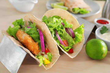 Holder with delicious fish tacos on wooden table
